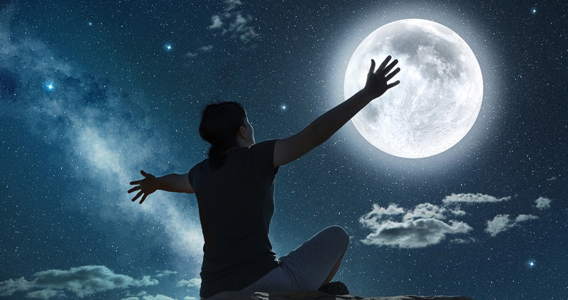 woman sitting and raising arms in the moonlight